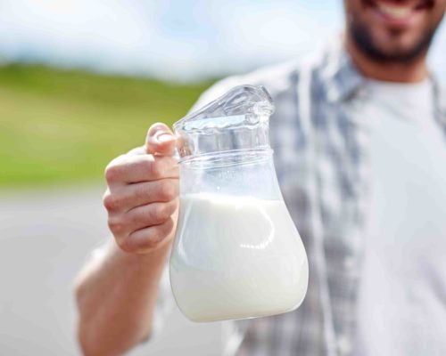 agriculture, farming, people and dairy concept - man or farmer with jug of milk at countryside